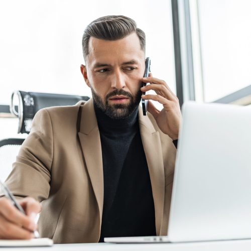 The businessman works in the office, speaks on the mobile phone and writes a note